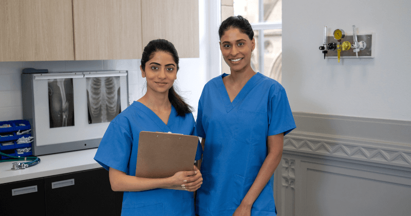 Two female nurses standing in front of a X-Ray wearing scrubs