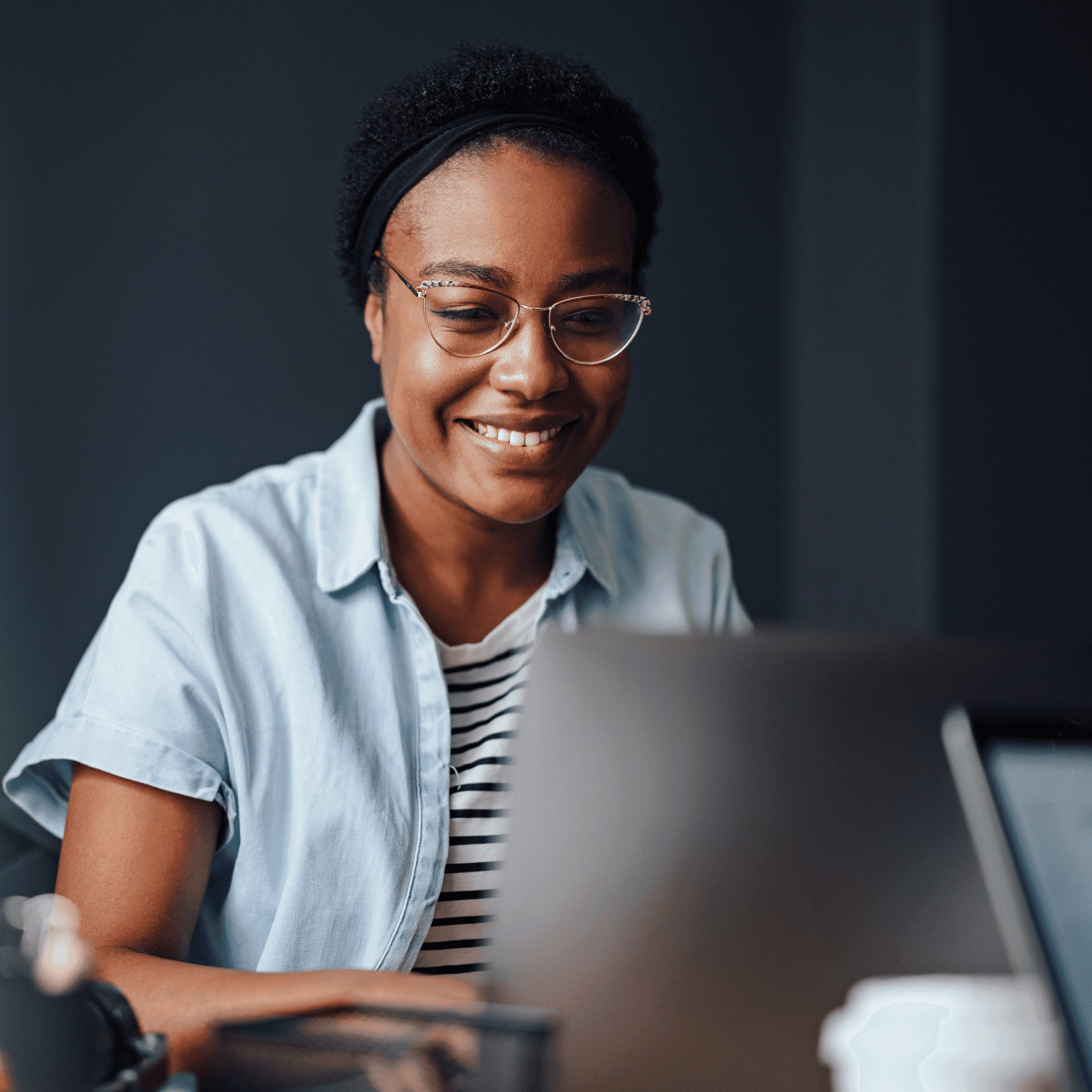 A black woman wearing glasses, reading something on a laptop